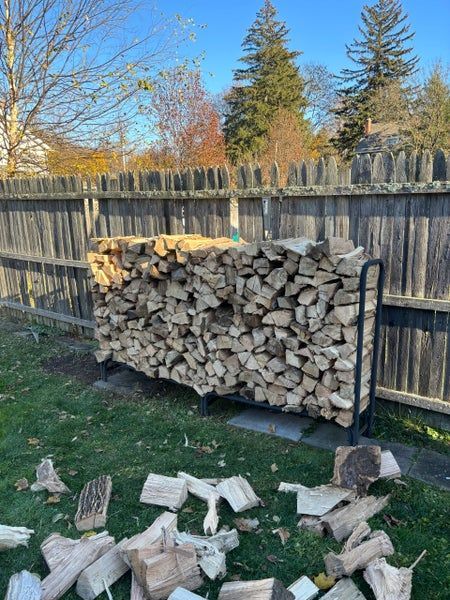 Stacked chopped firewood logs in warm brown tones, tightly piled together.