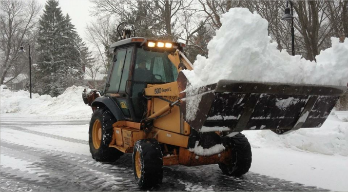 Yellow snowplow clearing a snowy road, pushing a large pile of snow.