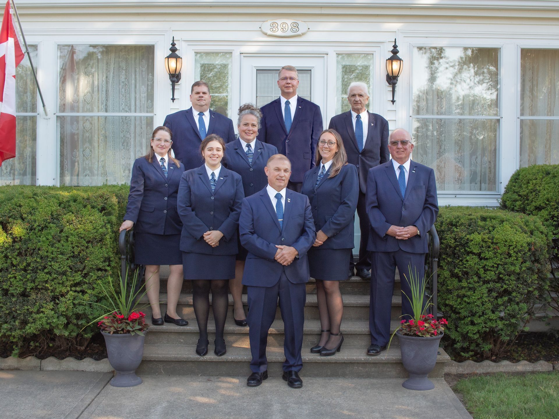 A group of eight professionals in matching blue suits stand on the front steps of a building with white trim.