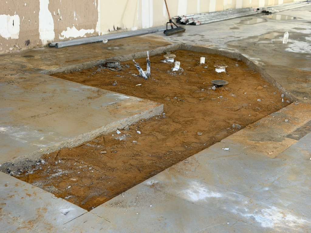 Wet brown stain on a concrete floor inside a room near a damaged wall.