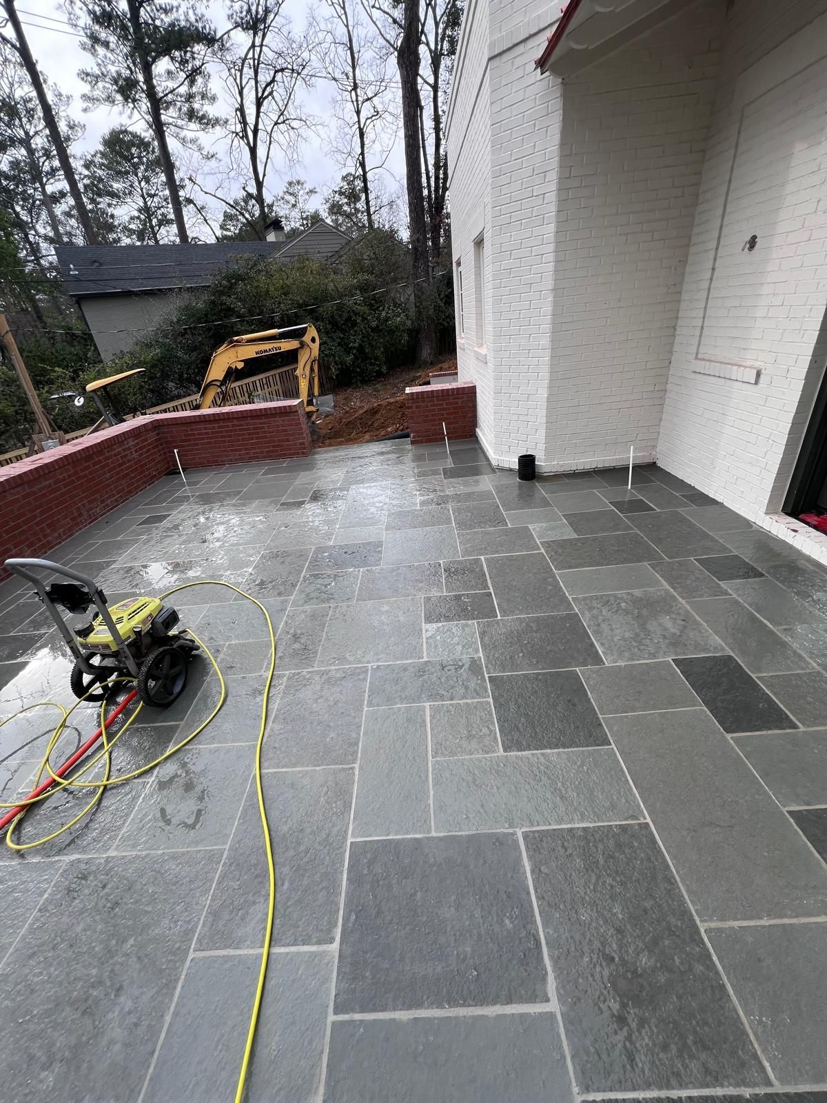 Gray stone patio with a pressure washer, bordered by red brick and white house walls