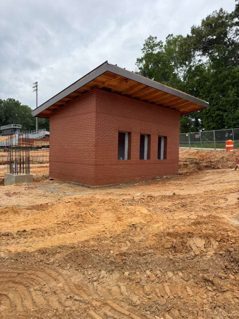 Small red-brick utility building with a sloped roof on a muddy construction site.