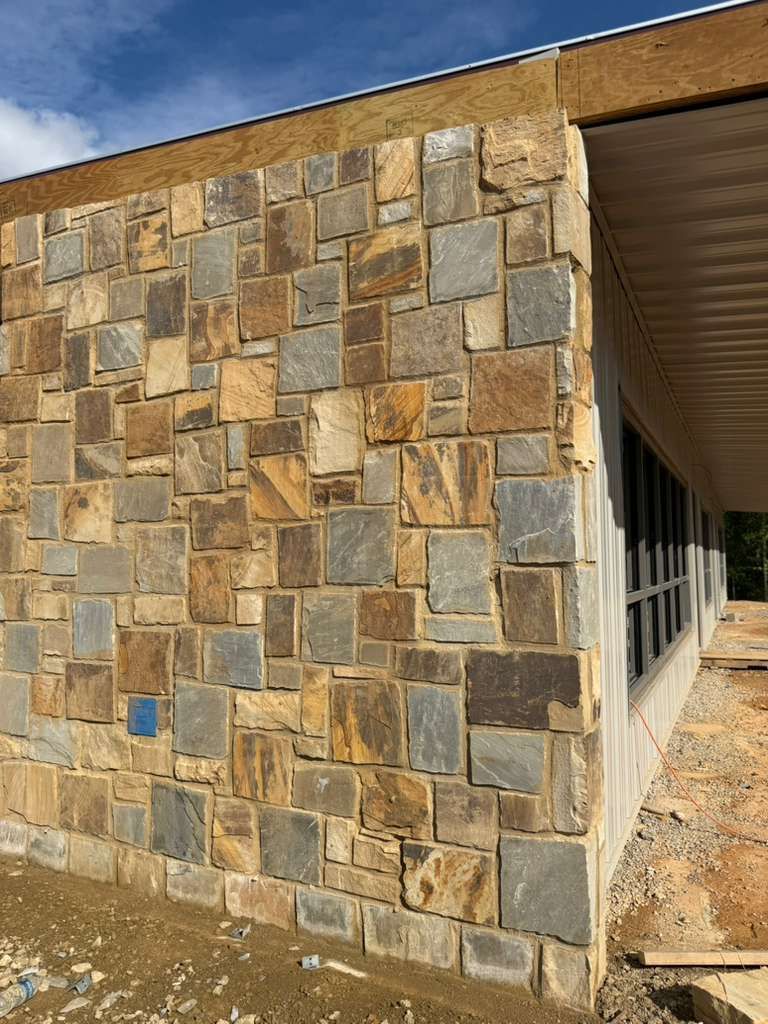 Stone-clad building corner beside a covered walkway and windows, with a textured tan and gray facade.