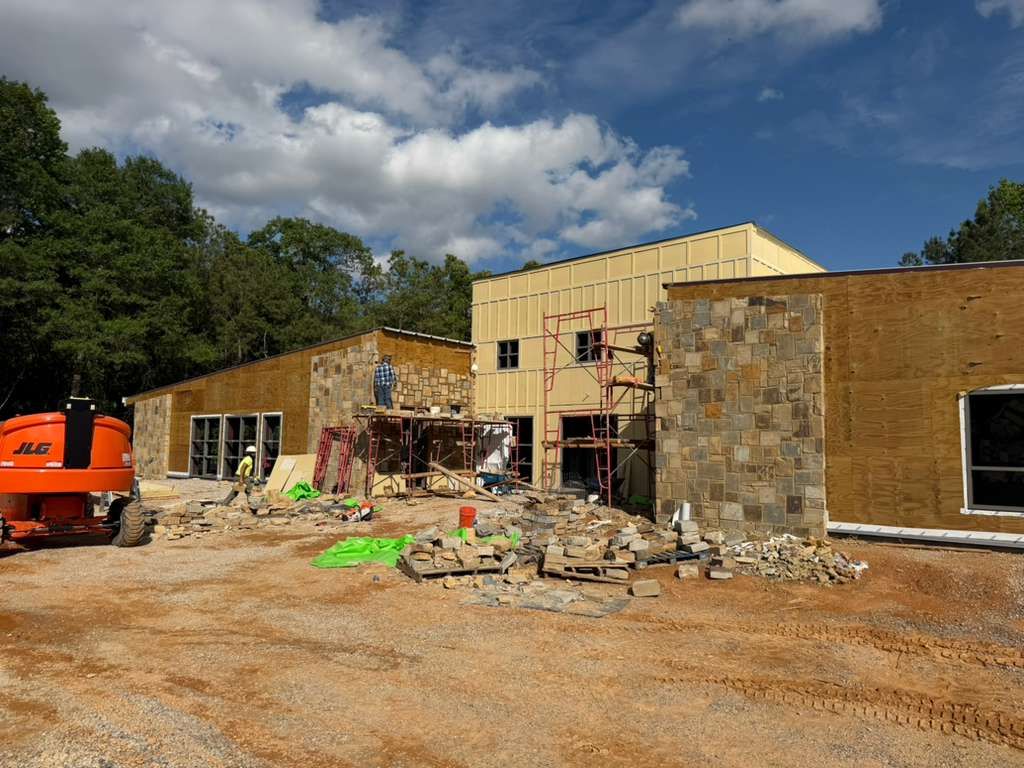 Construction site with partially built brick and stone building, orange excavator, and cloudy blue sky