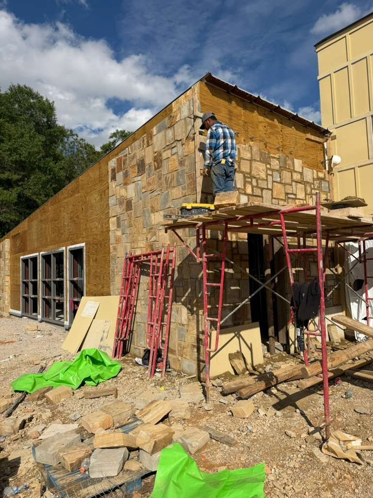 Stone building under construction with scaffolding, rubble, and a worker at an upper opening