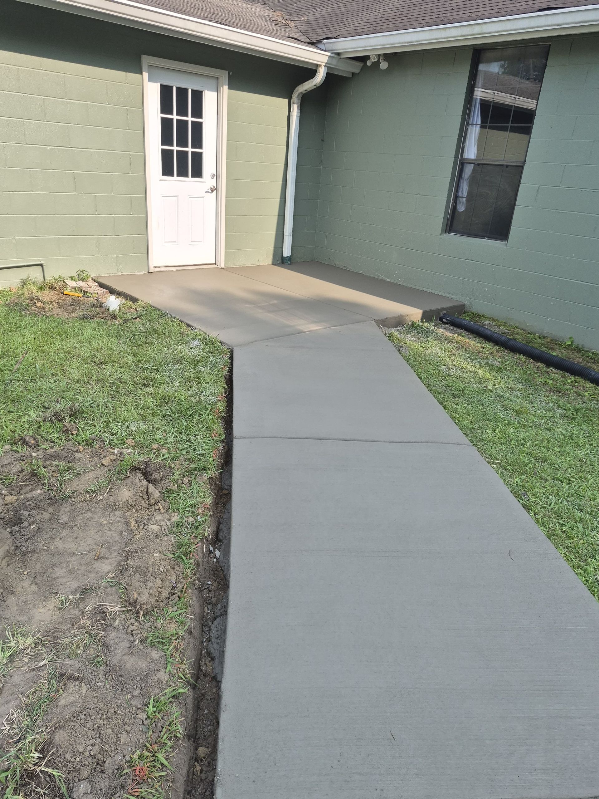 Concrete walkway leading to a white door beside a green house and grass lawn