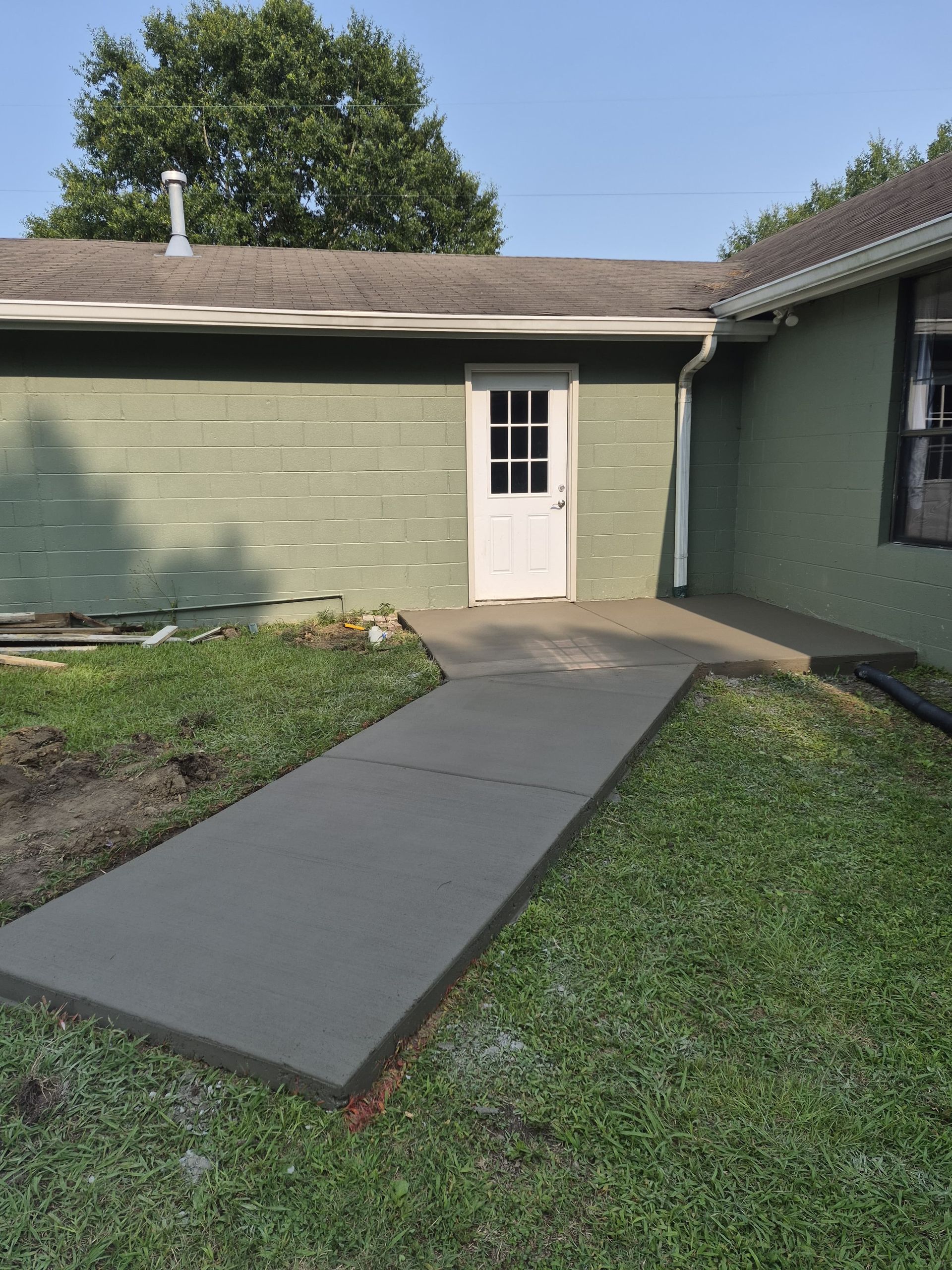 Small front yard with a concrete walkway leading to a white door on a green house.
