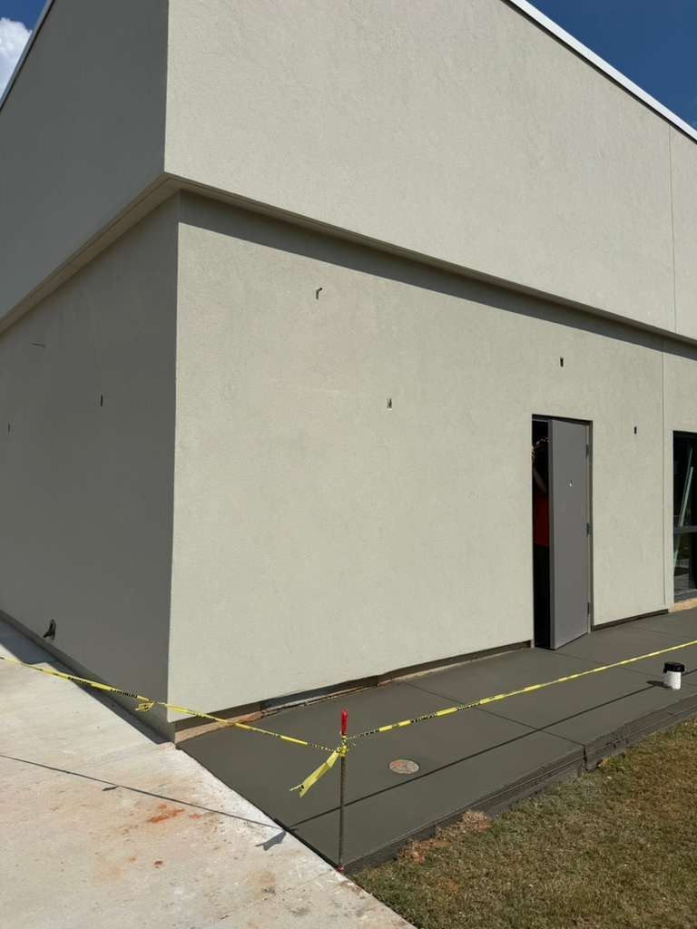 Exterior corner of a beige building with a gray ramp, doorway, and yellow caution tape on the ground