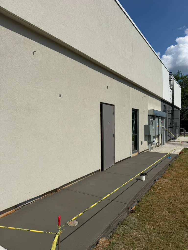 Side view of a white building with a gray door and walkway marked by yellow caution tape