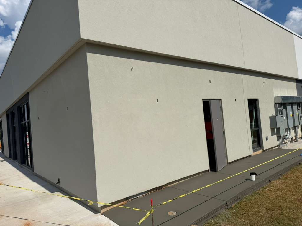 Exterior of a beige industrial building with windows, doors, and a paved walkway under a clear sky