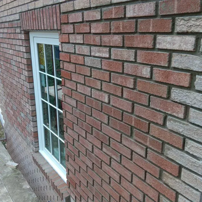 Brick wall with a white-framed window and sloped stone ledge on the side of a building