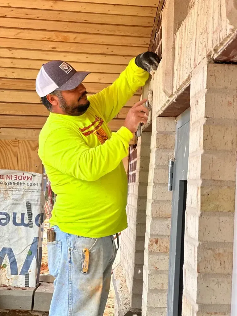 Worker in a neon yellow shirt installs trim on a wooden building frame.