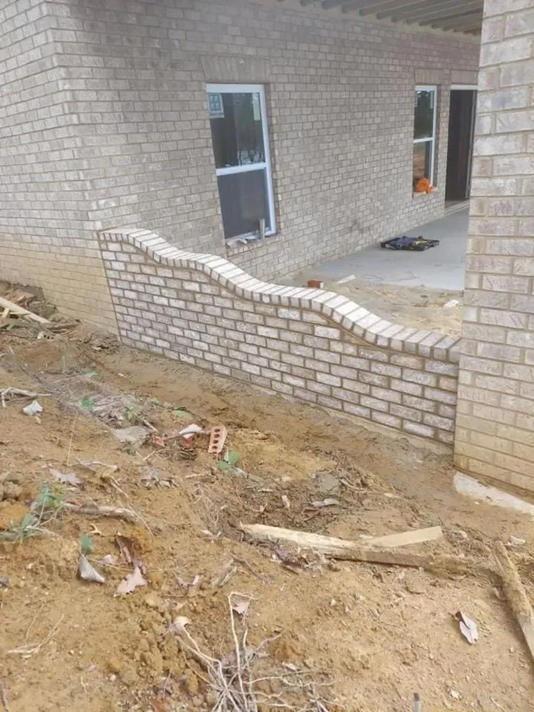Partially built brick house with a damaged low wall and dirt debris in the foreground