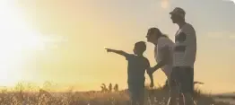 Silhouetted family pointing across a grassy field at sunrise
