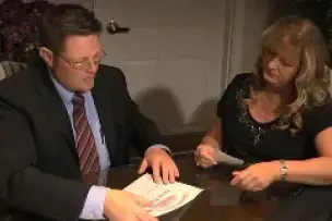 Two people at a table reviewing documents, one holding papers and the other pointing.