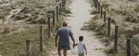 Two people walking hand in hand down a sandy path between fence posts