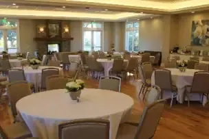 Empty banquet room with round tables, beige chairs, and warm wood flooring