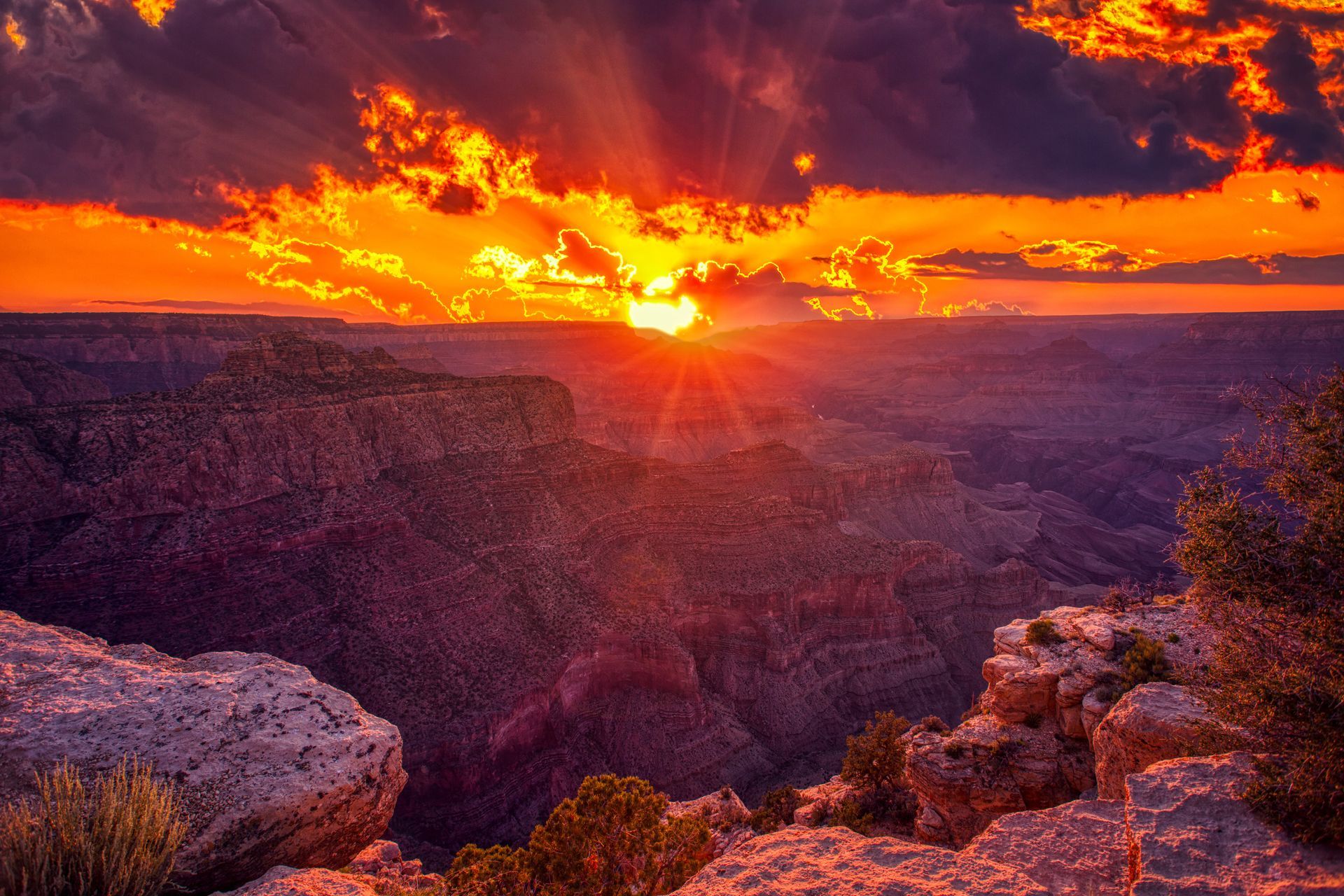 Sunset over a rugged canyon with fiery orange clouds and dark rocky cliffs