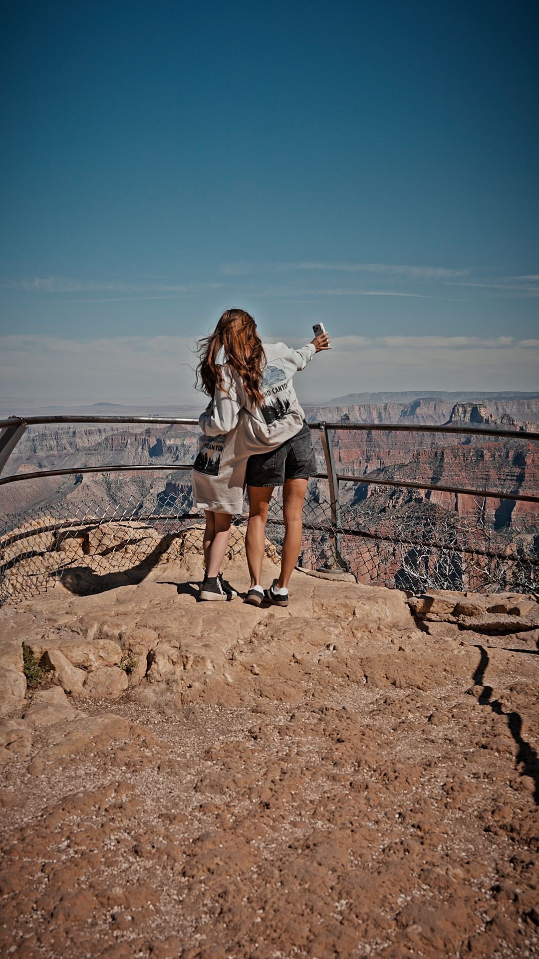 Person standing at a canyon overlook with a backpack, facing the view under a clear blue sky.