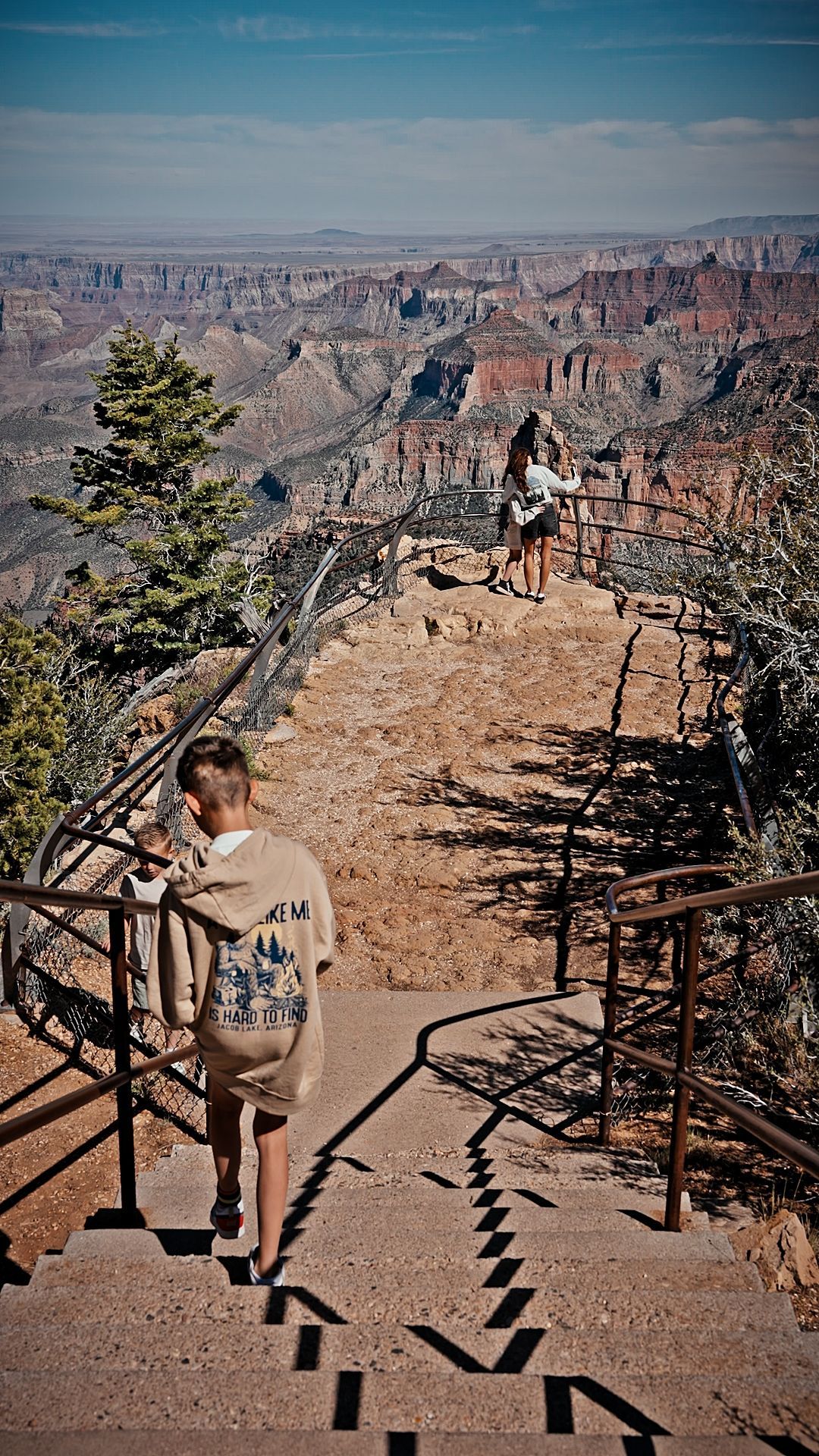 Hiker descending steps overlooking a vast red-rock canyon under a clear blue sky