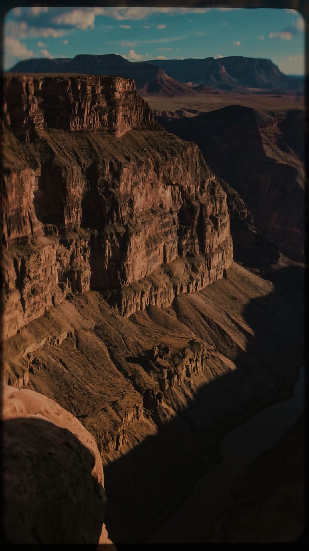 Sunlit red rock canyon cliffs under a blue sky, with deep shadows in the foreground