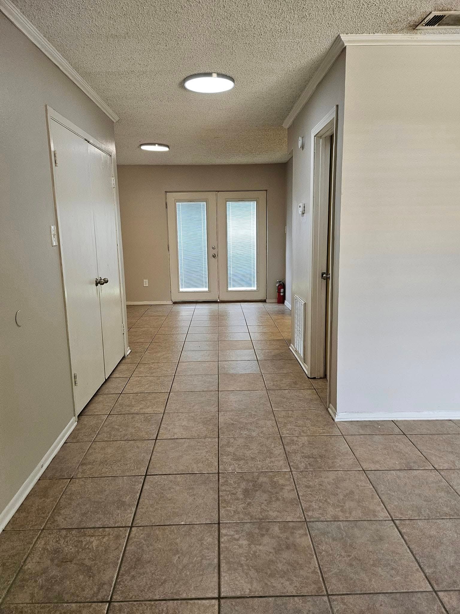 A long hallway with tile floors and sliding glass doors leading to a living room.