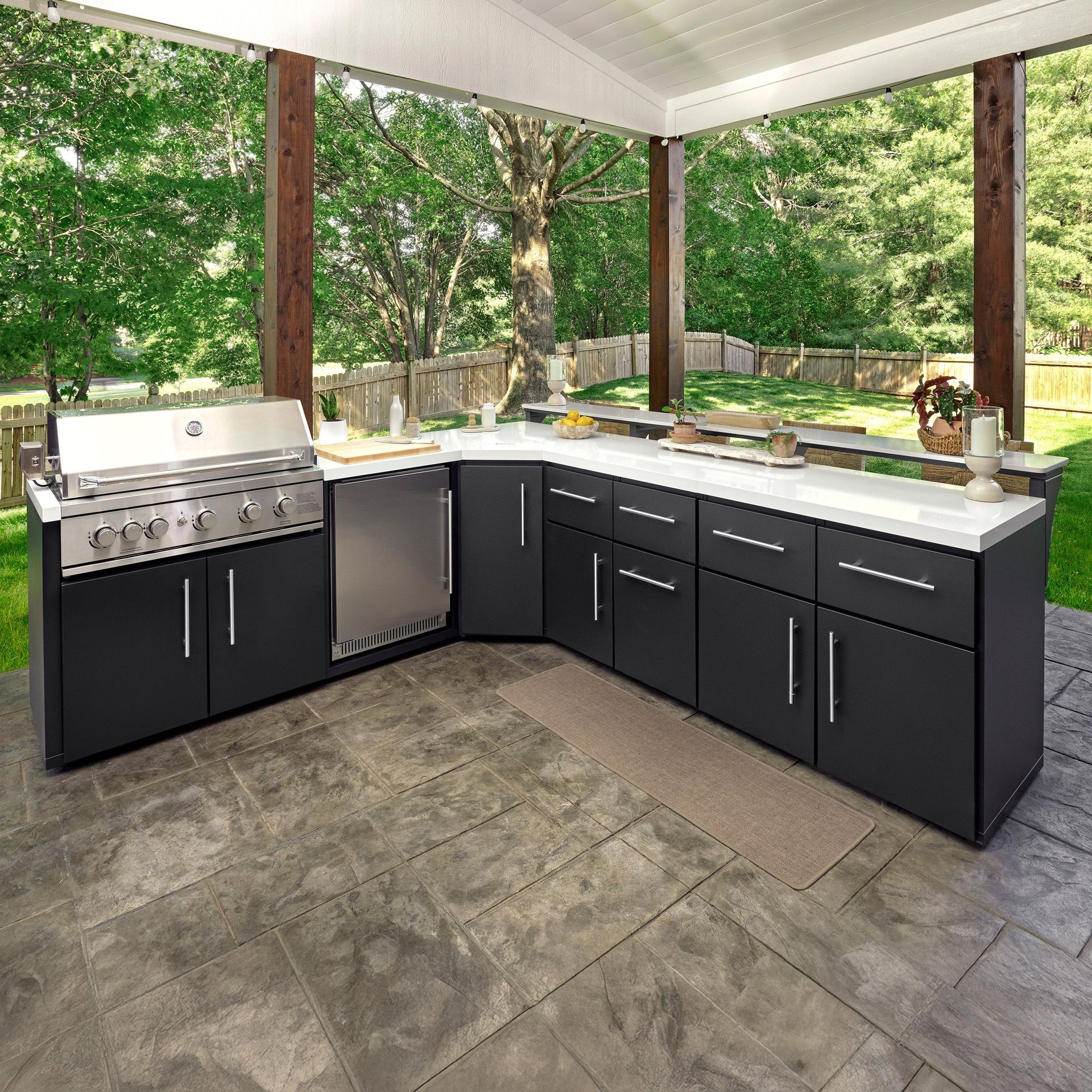 Outdoor kitchen with black cabinets, white countertop, stainless steel grill and fridge, gray patio.