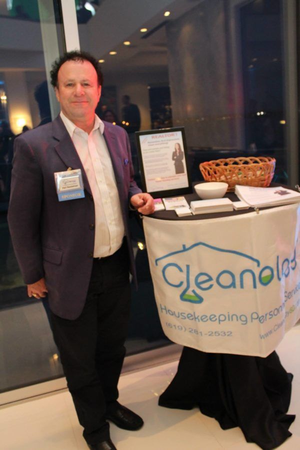 Man standing beside a Cleanology housekeeping services display table with brochures and a basket at an indoor event