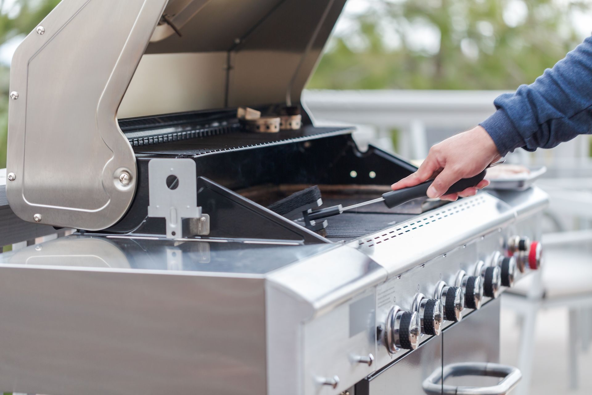 Person cleaning a stainless steel gas grill outdoors