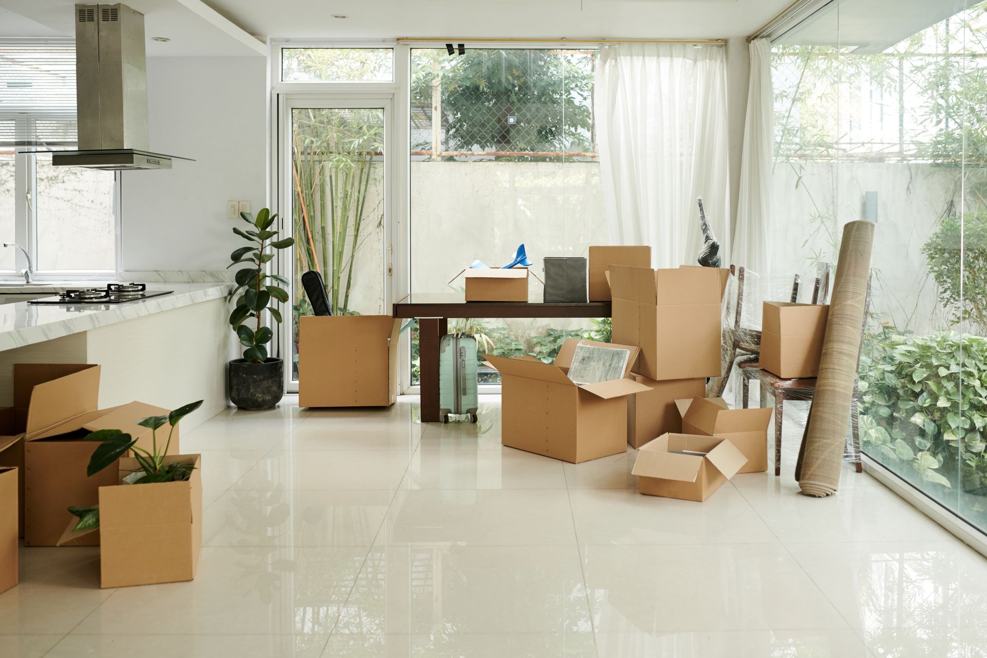 Bright empty living room with moving boxes, unpacked chairs, and sunlight through large windows