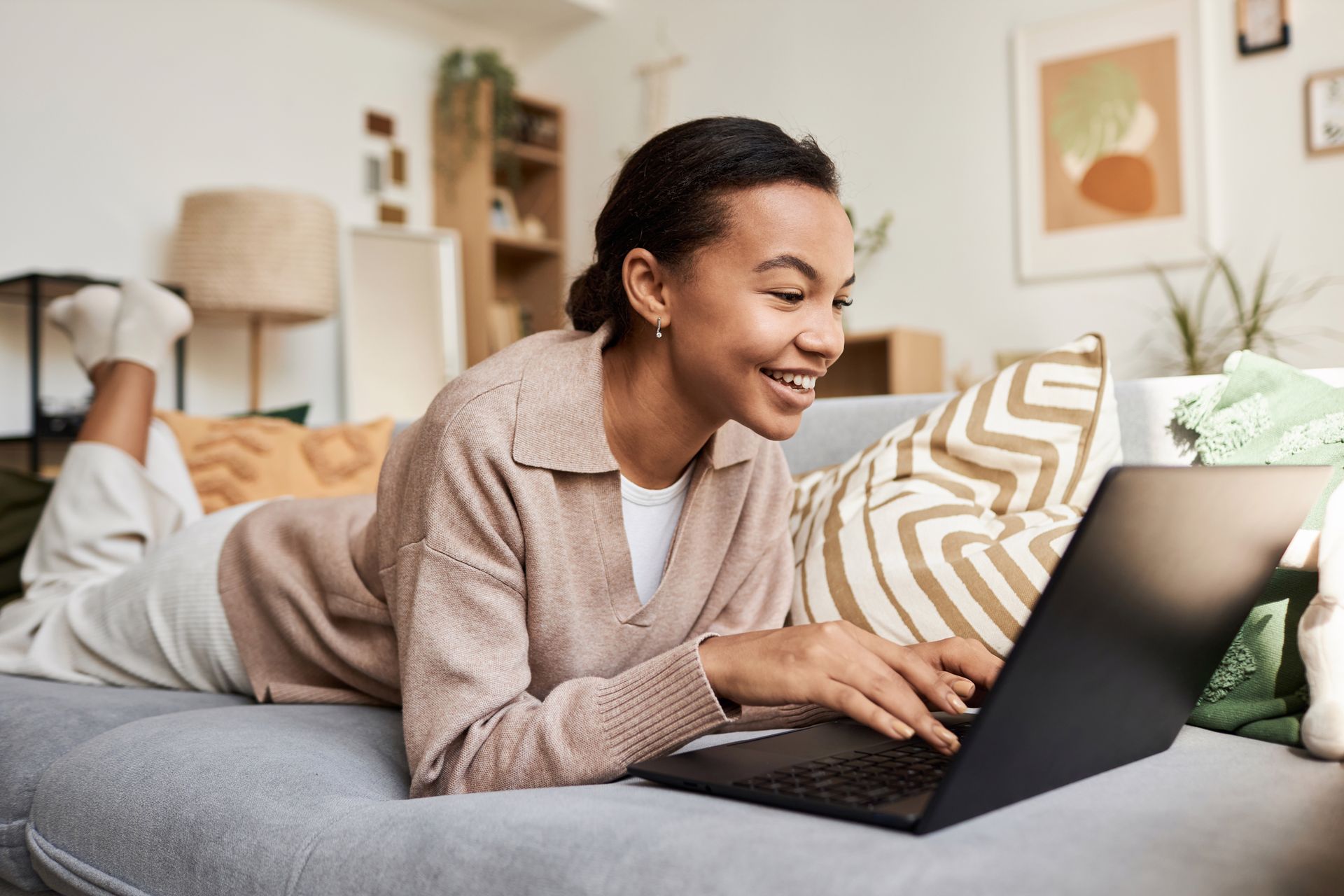 Person smiling while using a laptop on a couch in a bright living room