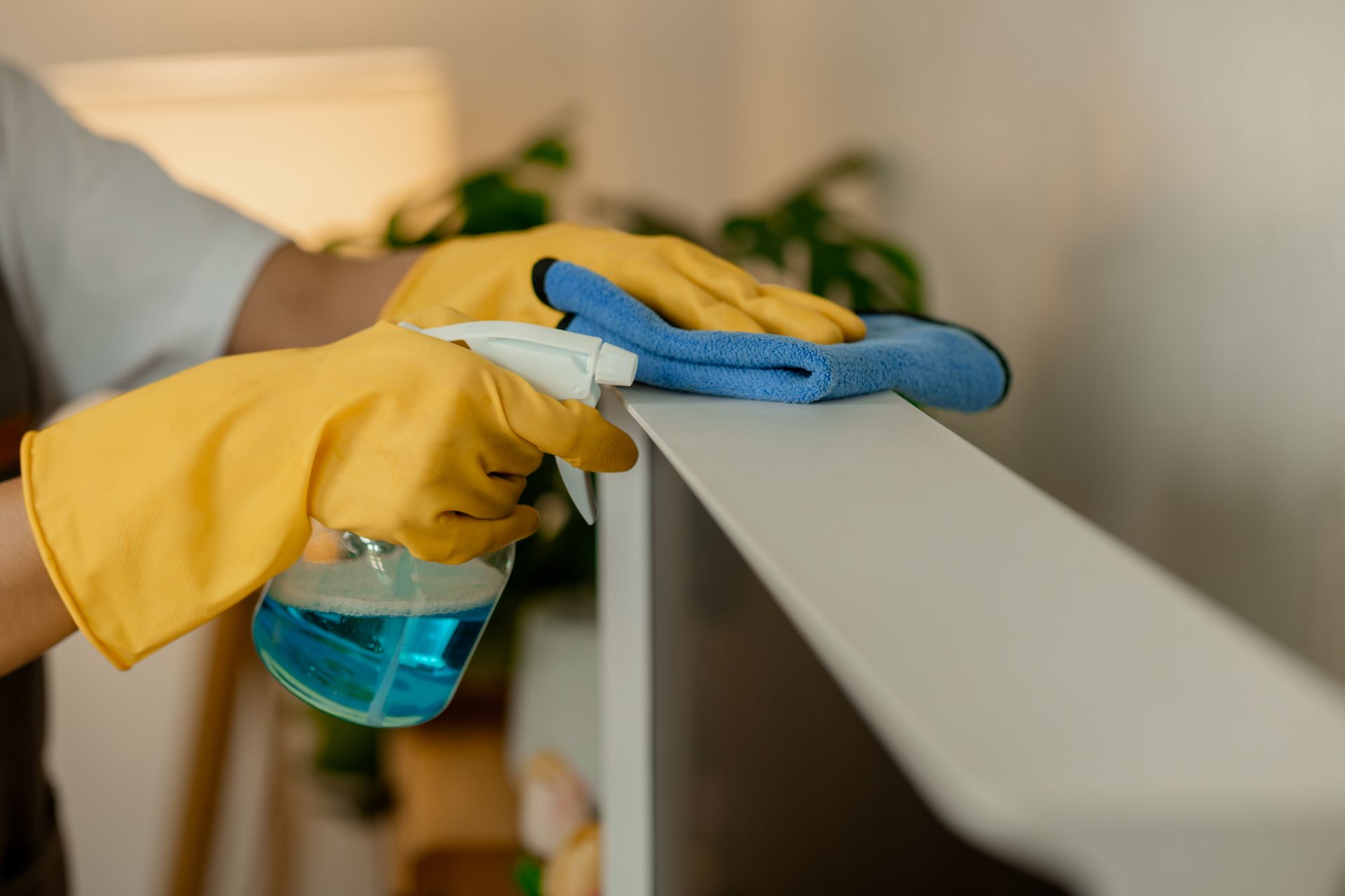 Person in yellow gloves spraying and wiping a white railing with blue cloths