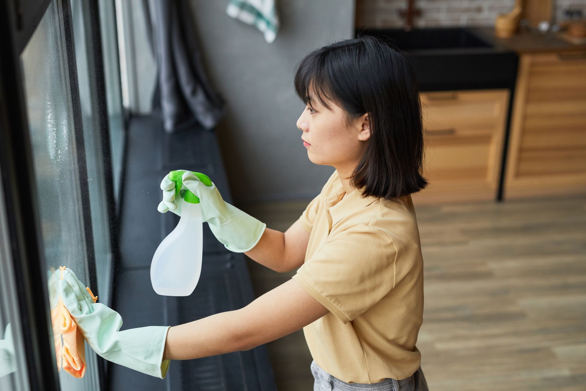 Woman cleaning a window with a spray bottle and cloth indoors