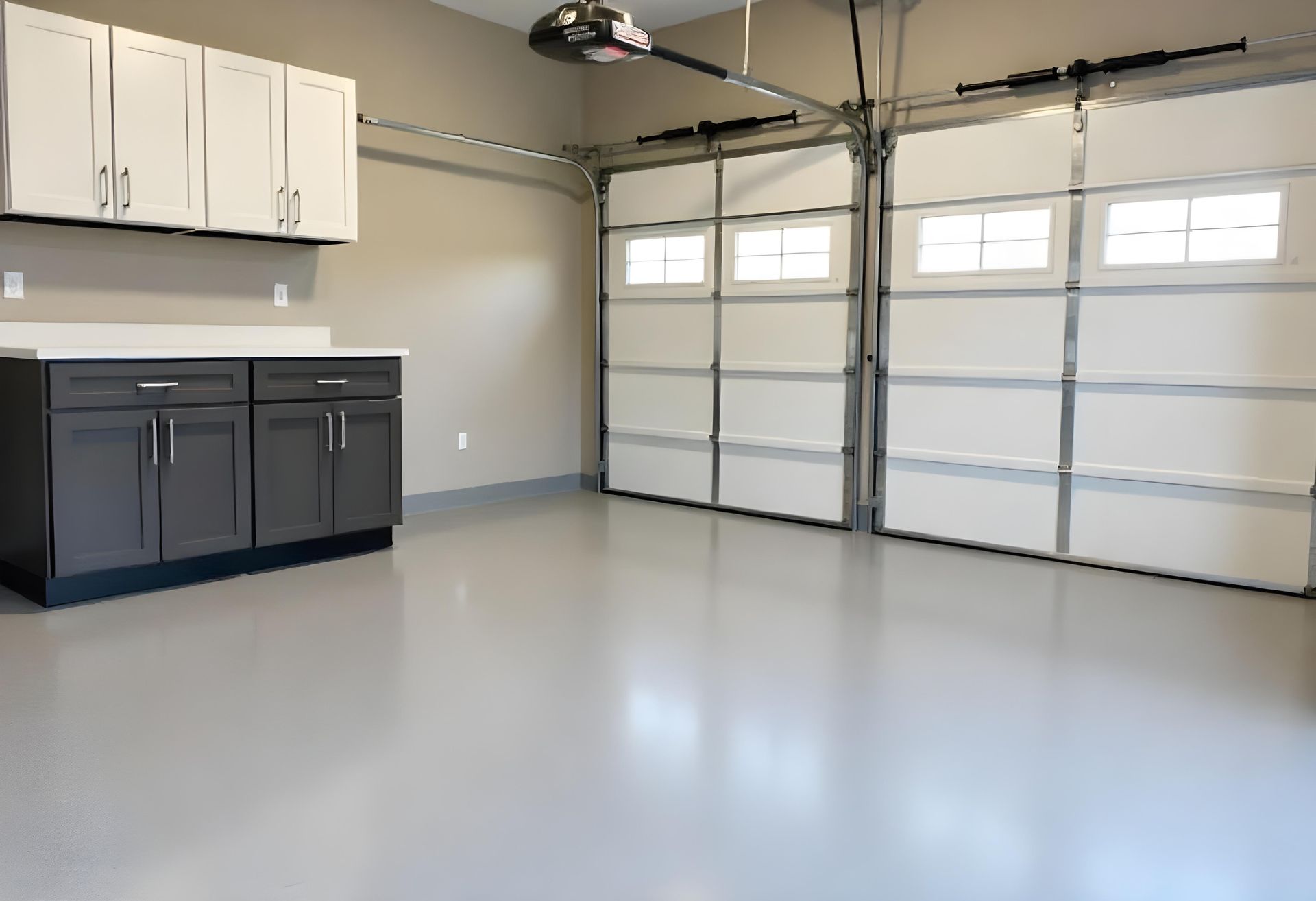 Empty garage with gray epoxy floor, white cabinets, and closed double garage doors.