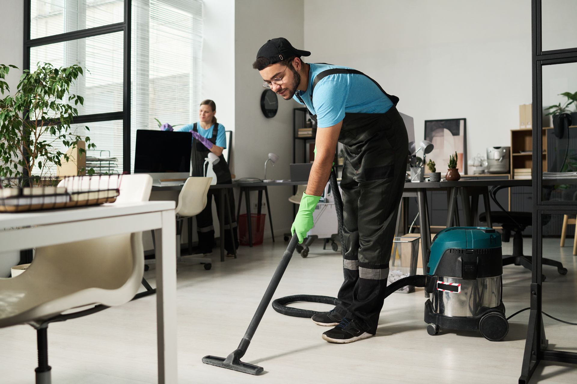 Janitor vacuuming a bright office floor beside a cleaning cart and supplies
