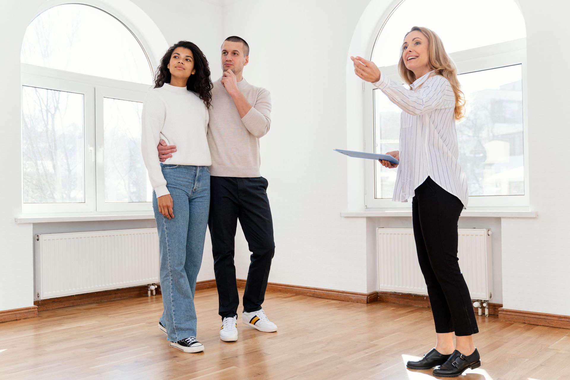 Three people standing in a bright empty room, one pointing while holding a clipboard