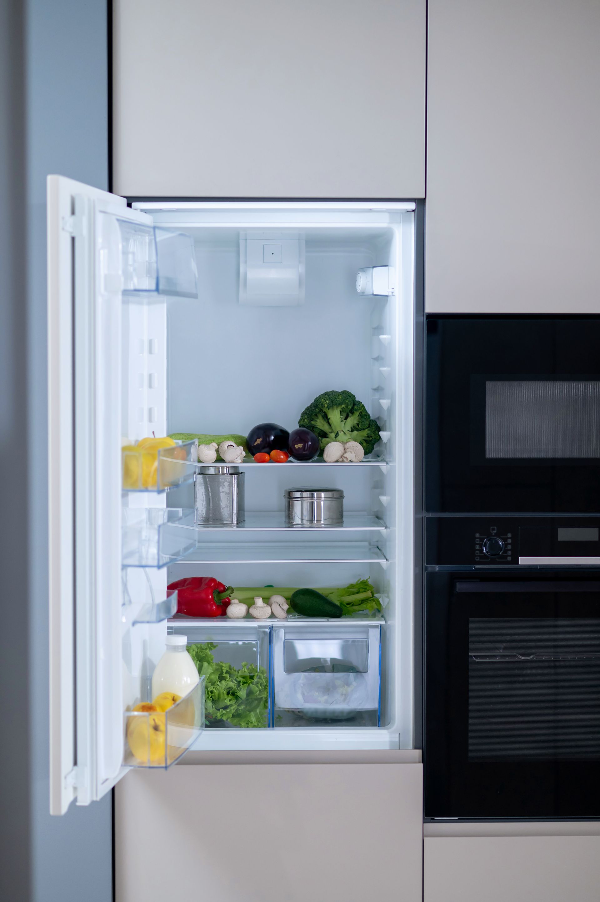 Open refrigerator in a modern kitchen, stocked with fruits, vegetables, and containers.