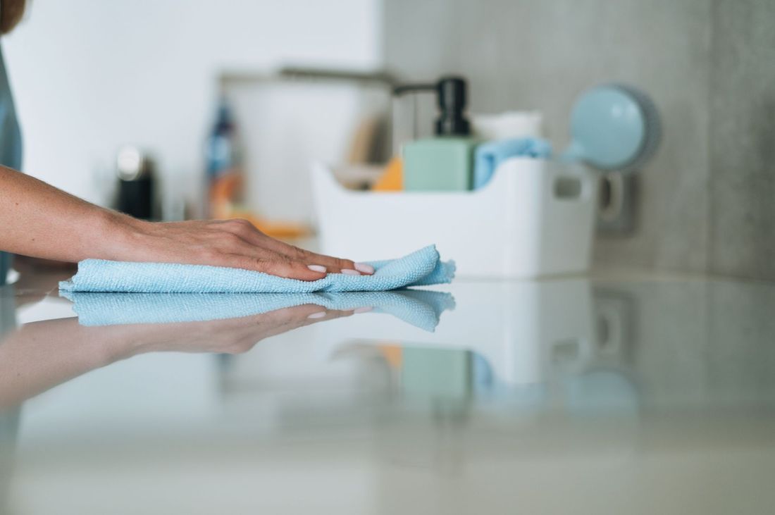 Hand wiping a kitchen counter with a blue cloth, cleaning supplies in the background