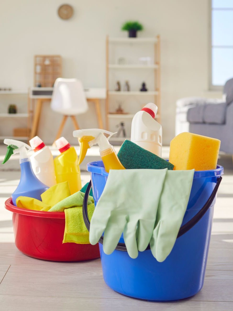 Cleaning supplies in colorful buckets with sprays, sponges, and gloves on a floor in a bright room