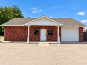 Brick building with white columns and a covered porch on a sunny day.
