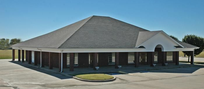 A single-story commercial building with a gray roof and brick facade under a clear blue sky.