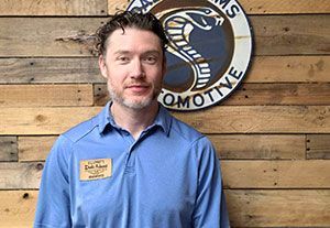 Man in a blue shirt standing before a wooden wall with a circular business sign