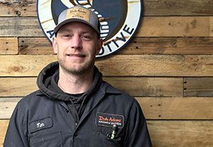 Man in a tan cap and dark jacket standing before a wooden wall and round business sign