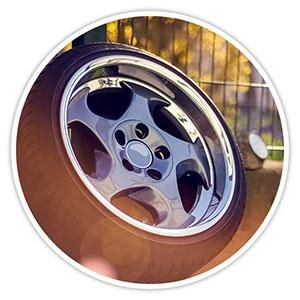 Chrome car wheel rim with black spokes on a tire, shot close-up outdoors at sunset