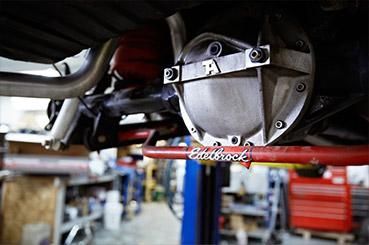 Close-up of a car differential under a vehicle in a garage, with tools blurred in the background