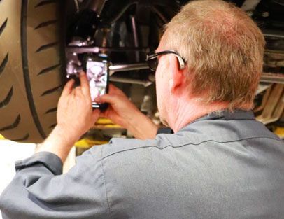 Mechanic photographing a car wheel with a smartphone under the vehicle