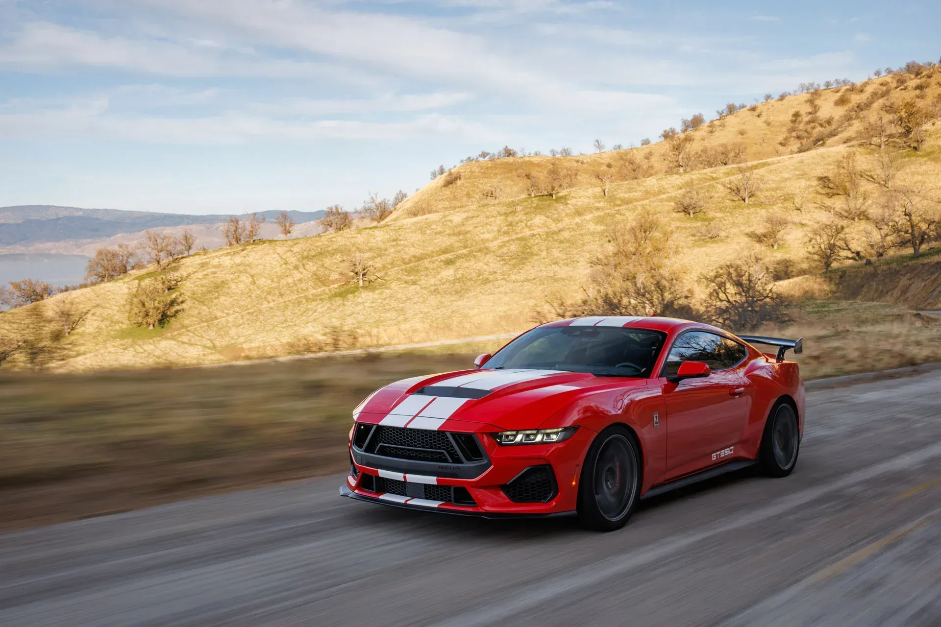 Red sports car driving on a winding road through dry hills under a clear sky