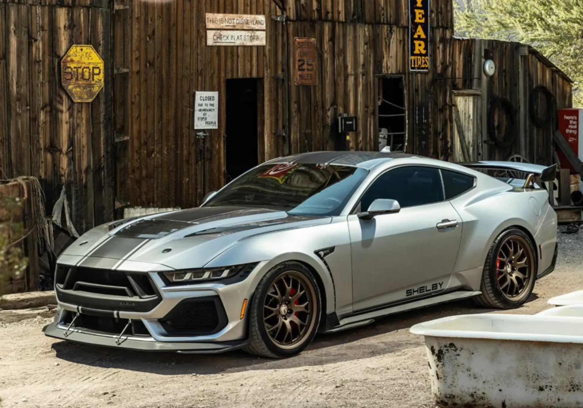 Silver sports car parked outside a rustic wooden building with a yellow sign.