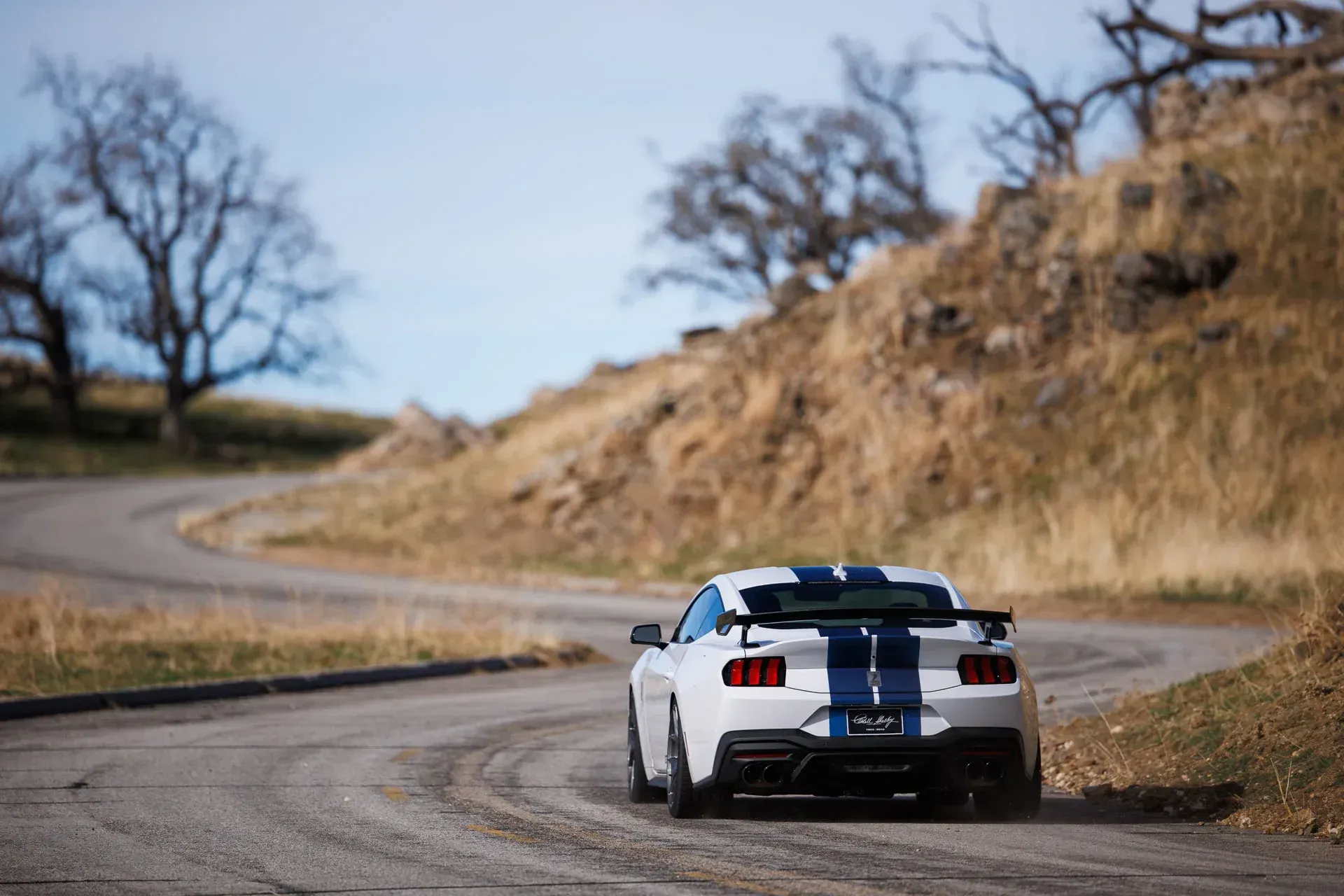 White sports car driving on a winding country road beside dry hills and trees