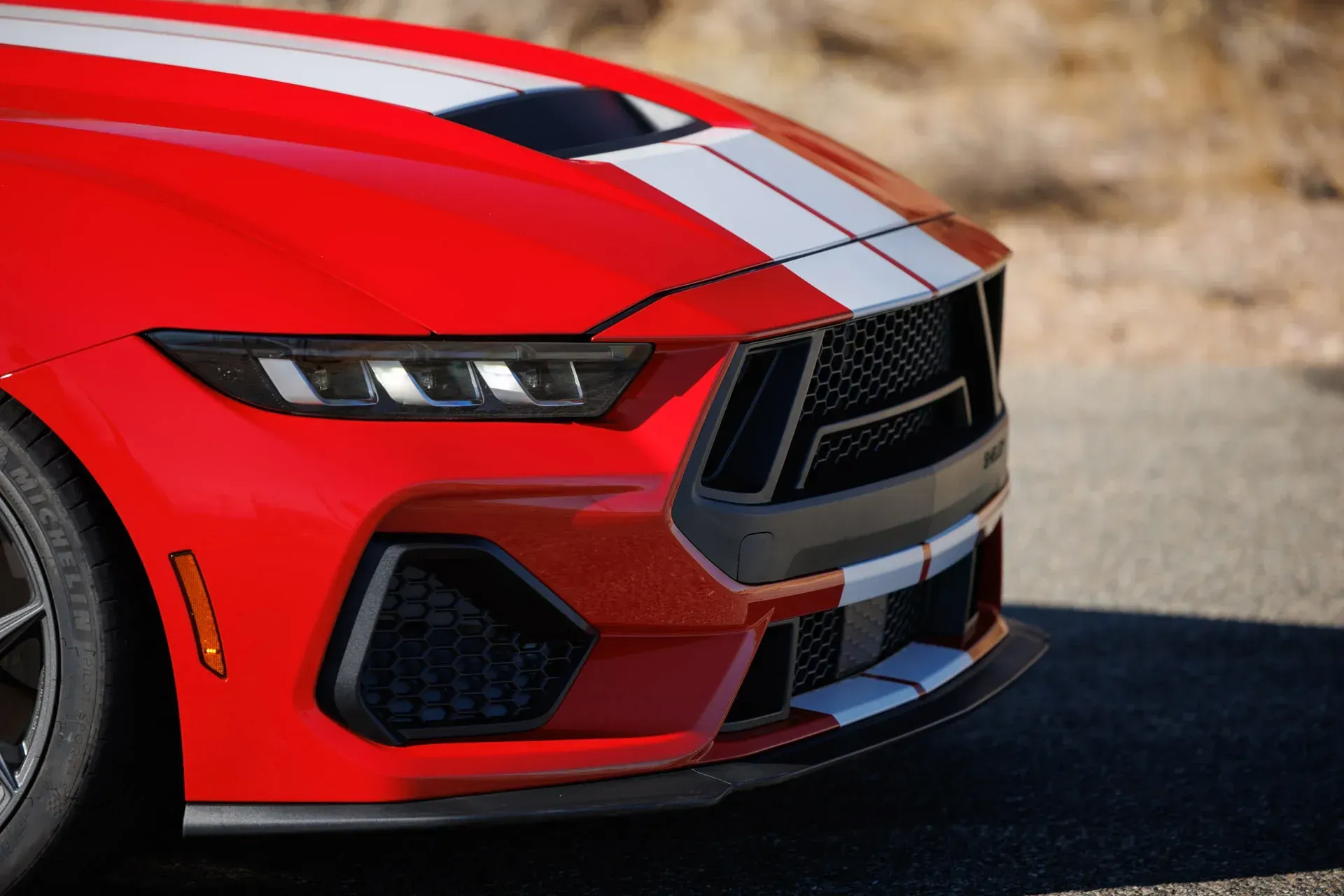 Red sports car front end with white racing stripes on a road